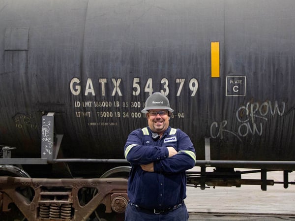 Smiling man in a Reworld hardhat standing in front of an oil tanker truck