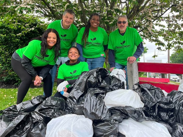 Group of smiling volunteers standing behind a pile of trash bags at a park clean-up