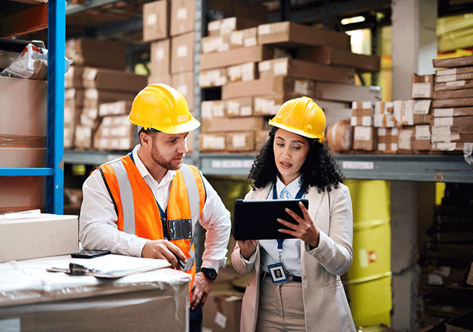 Man and woman in hardhats looking at a tablet in warehouse